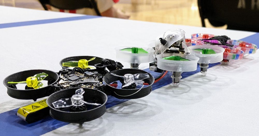Photo of three tiny whoop drones lined up to race at the Spring 2022 YDSC State Championships in Richfield, Minnesota, United States, by Nic Rosenau. 2022. CC BY 4.0.