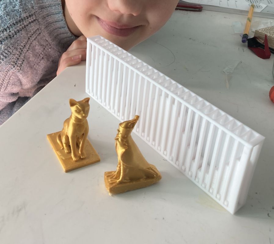 A partial face looking toward gold colored 3D printed statues of a cat and a falcon.