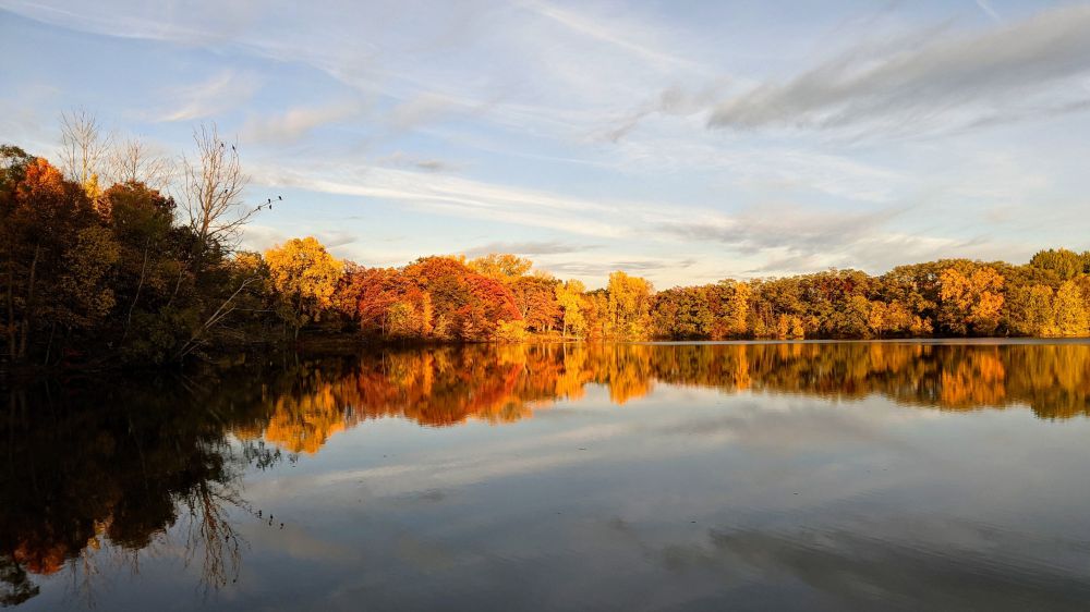 On a cloudy day, vibrant fall colors are reflected in Silver Lake at Silverwood Park, Saint Anthony Village, Minnesota, USA.