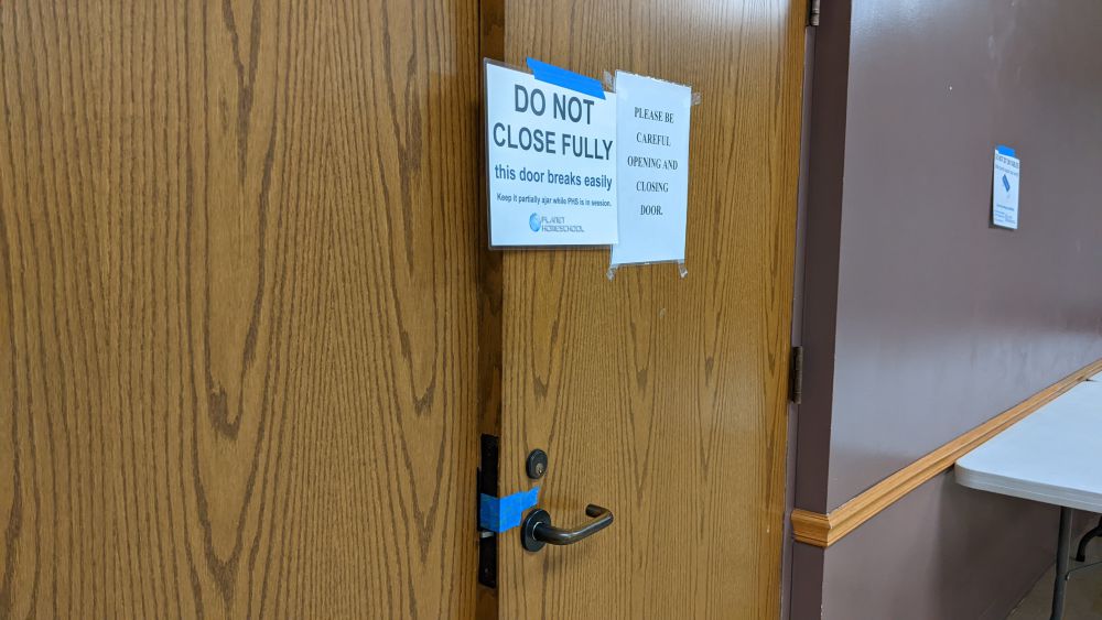 Fellowship Hall Storage Room door closed with sign and blue tape over latch