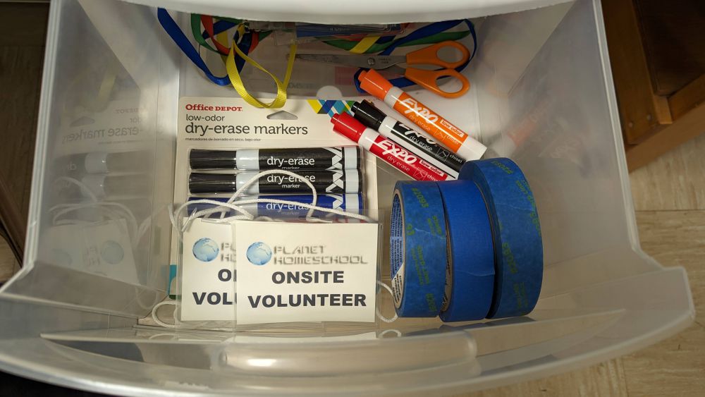 Onsite Volunteer Badges, blue tape, and dry erase markers in a drawer